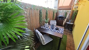 Een terras met een tafel, stoelen, een barbecue en een bamboehek.