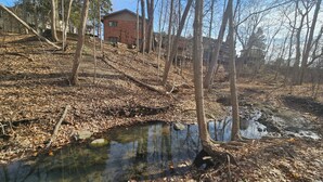 A natural landscape with a small stream, trees, and a building in the background. - Serene 4-bedroom house with brook and forest in charming Racine (Racine)
