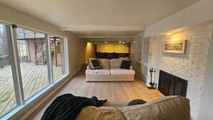 A cozy living room with a sofa, fireplace, and large windows overlooking a deck. - Serene 4-bedroom house with brook and forest in charming Racine (Racine)