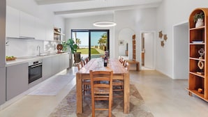 Een moderne keuken met een eetgedeelte, met een grote houten tafel en stoelen, een inbouwoven en uitzicht op de omgeving.