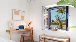 Een slaapkamer met een bed, een bureau met stoel, een raam met uitzicht op groen en een bank.