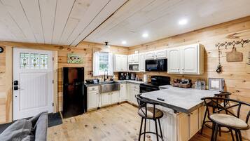 A kitchen with wooden walls, white cabinets, a black refrigerator, a microwave, a sink, and a bar area with stools.