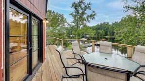 Une terrasse avec une table et des chaises, donnant sur un lac où l’on peut voir des bateaux et des arbres.