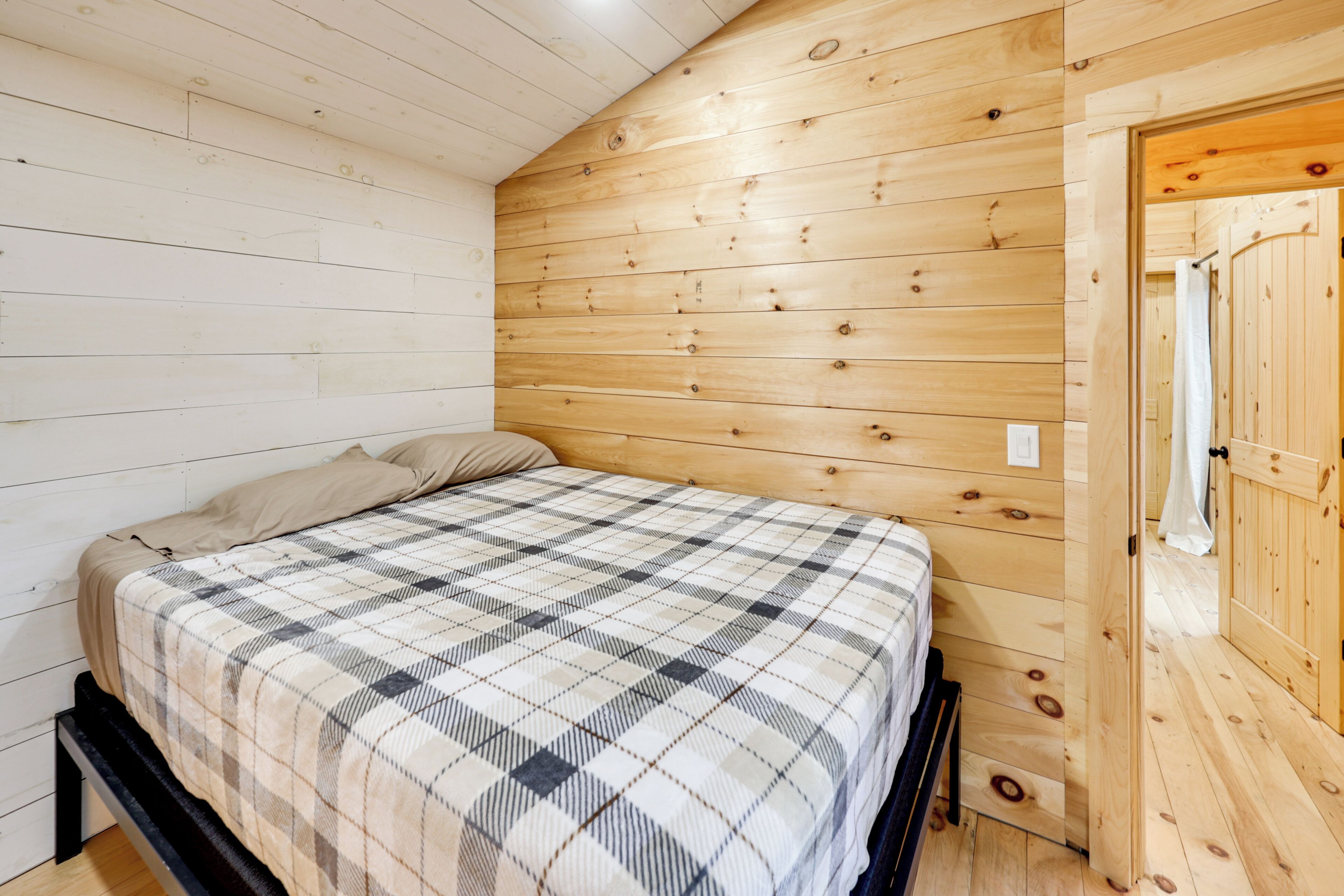 Una habitación con cama, paredes de madera y una puerta.