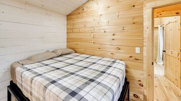 Una habitación con cama, paredes de madera y una puerta.