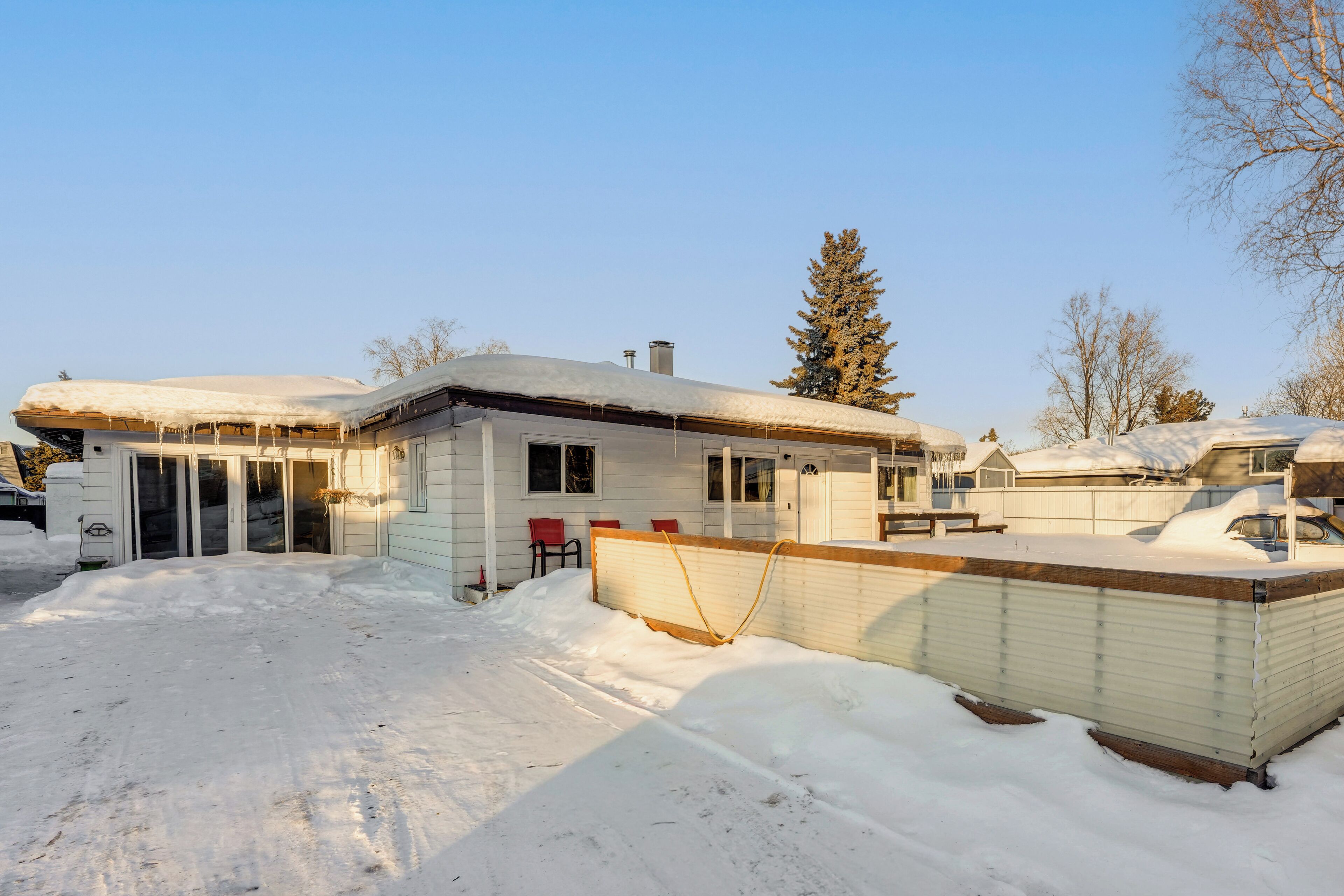 A house with a snow-covered roof and a fenced backyard.