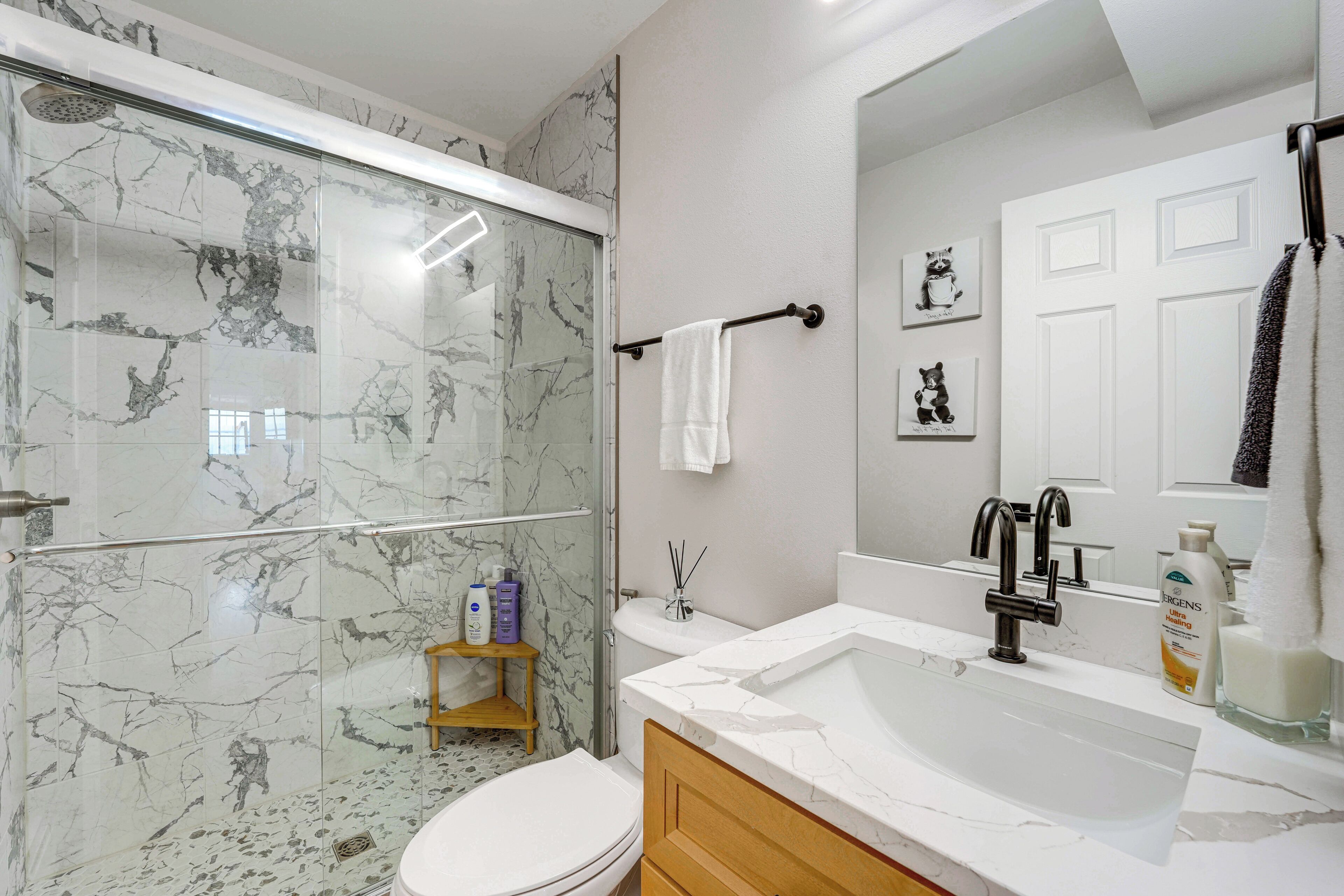 A bathroom with a glass shower enclosure, a white toilet, a vanity with a sink, and a mirror.