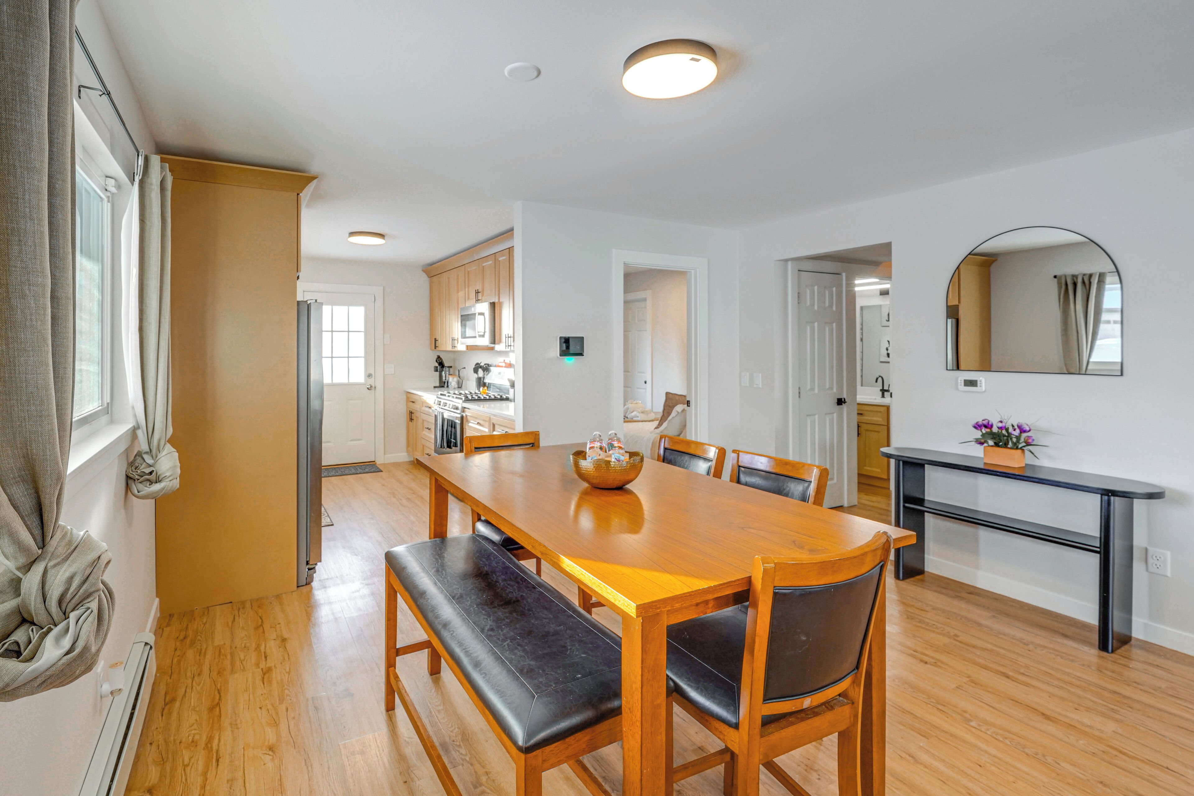 A spacious dining area with a wooden table and benches, a kitchen in the background, and a mirror on the wall.