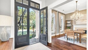 Una habitación amplia con un gran comedor de madera, una araña y vistas al exterior a través de un ventanal.