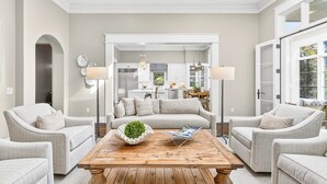 Amplia sala de estar con una mesa de centro de madera, dos sillones y un sofá. Se ve una cocina a través de un vano abierto.