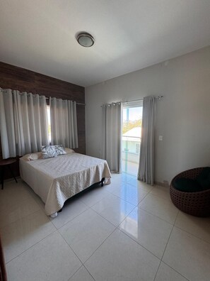 Une chambre moderne avec un grand lit, un petit coin salon circulaire et un balcon agrémenté de rideaux.