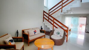 A spacious living area with a wooden staircase, a sofa set, a round wooden coffee table, and a wicker chair. - Casa Sol e Sal is the beach house with a pool for your family. (Prado)