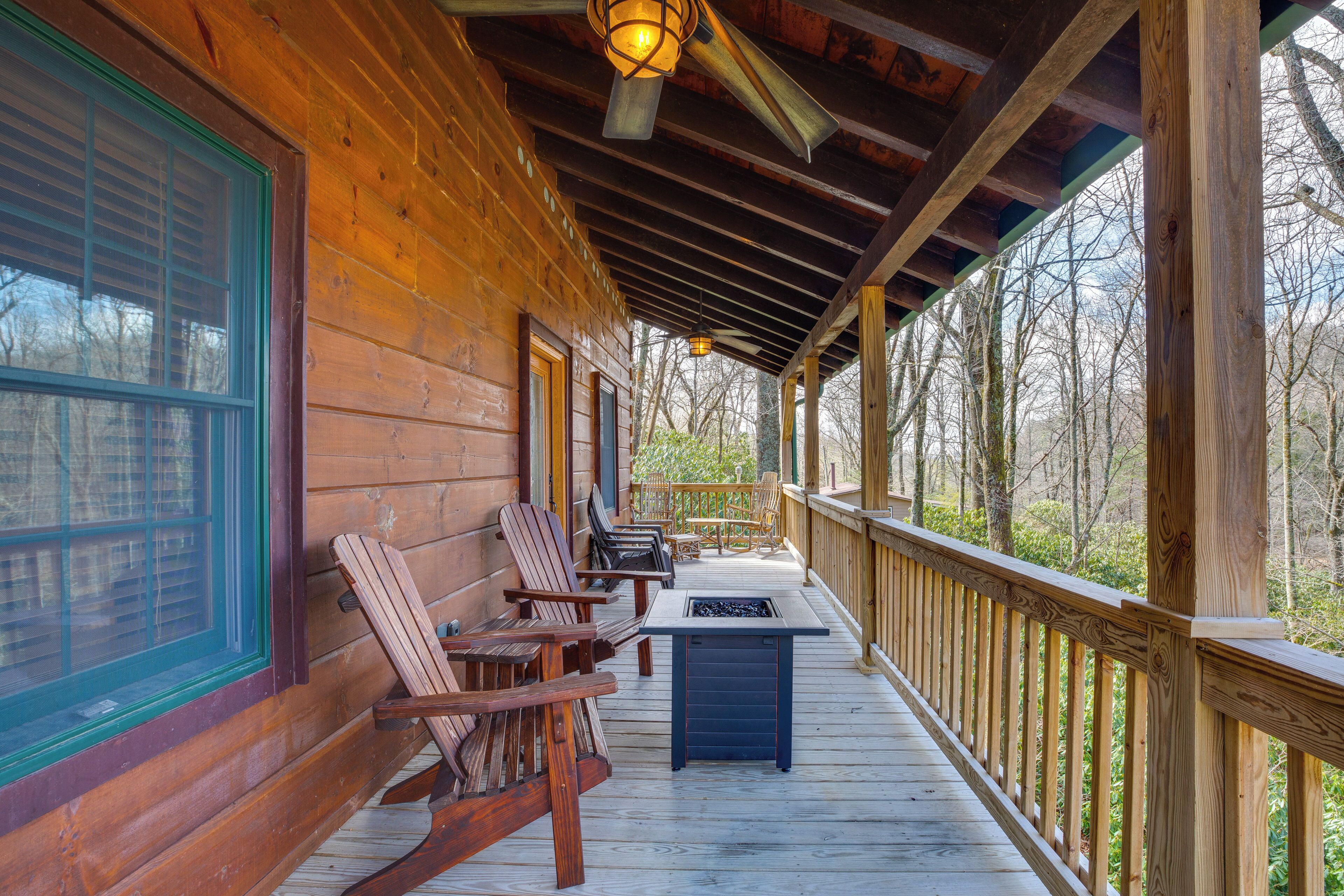 Une terrasse en bois avec des fauteuils Adirondack et une table, donnant sur une zone boisée.
