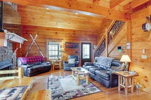 Ein gemütliches Blockhaus-Interieur mit Kamin, Ledersofas, einer Holztreppe und rustikaler Einrichtung.