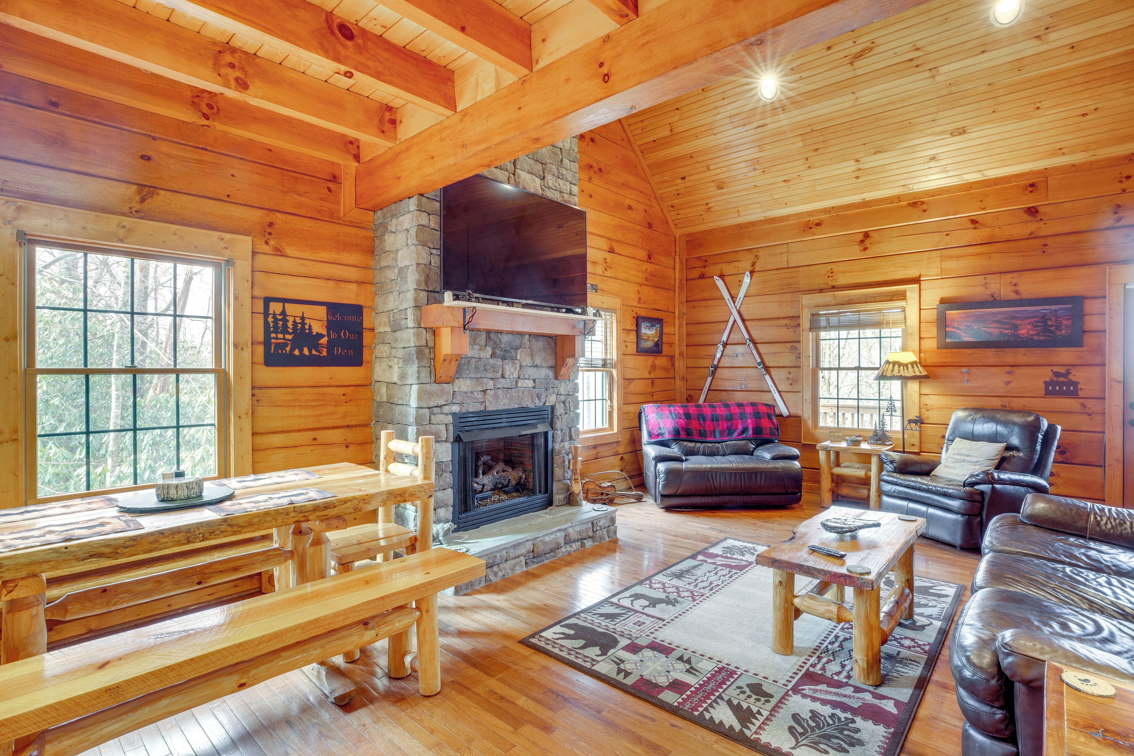 A cozy cabin interior with a stone fireplace, wooden furniture, and a large window.