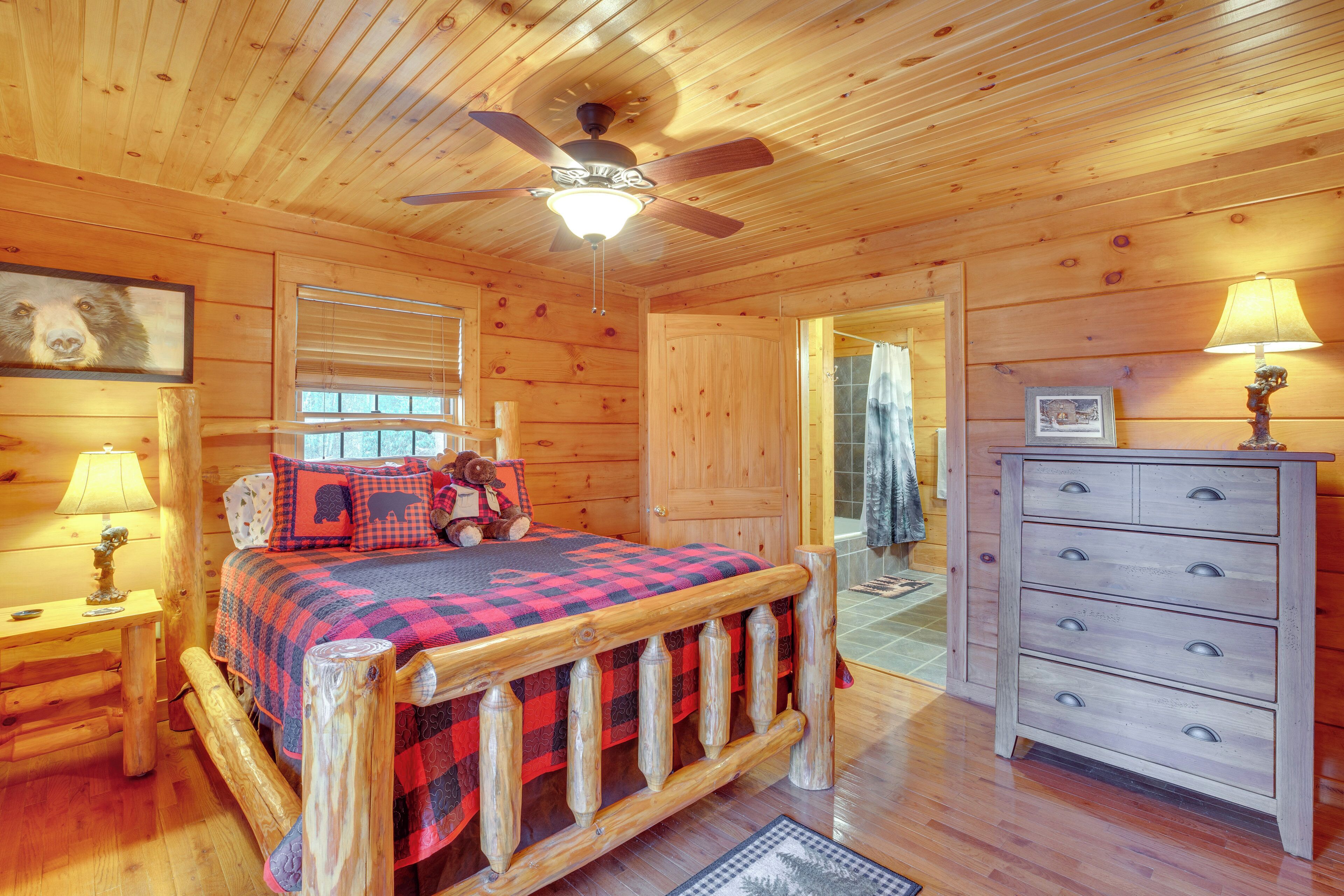 A wooden cabin interior with a bed, dresser, and ceiling fan.