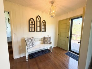 A room with a white bench, patterned pillows, a wooden door, and a ceiling light fixture.