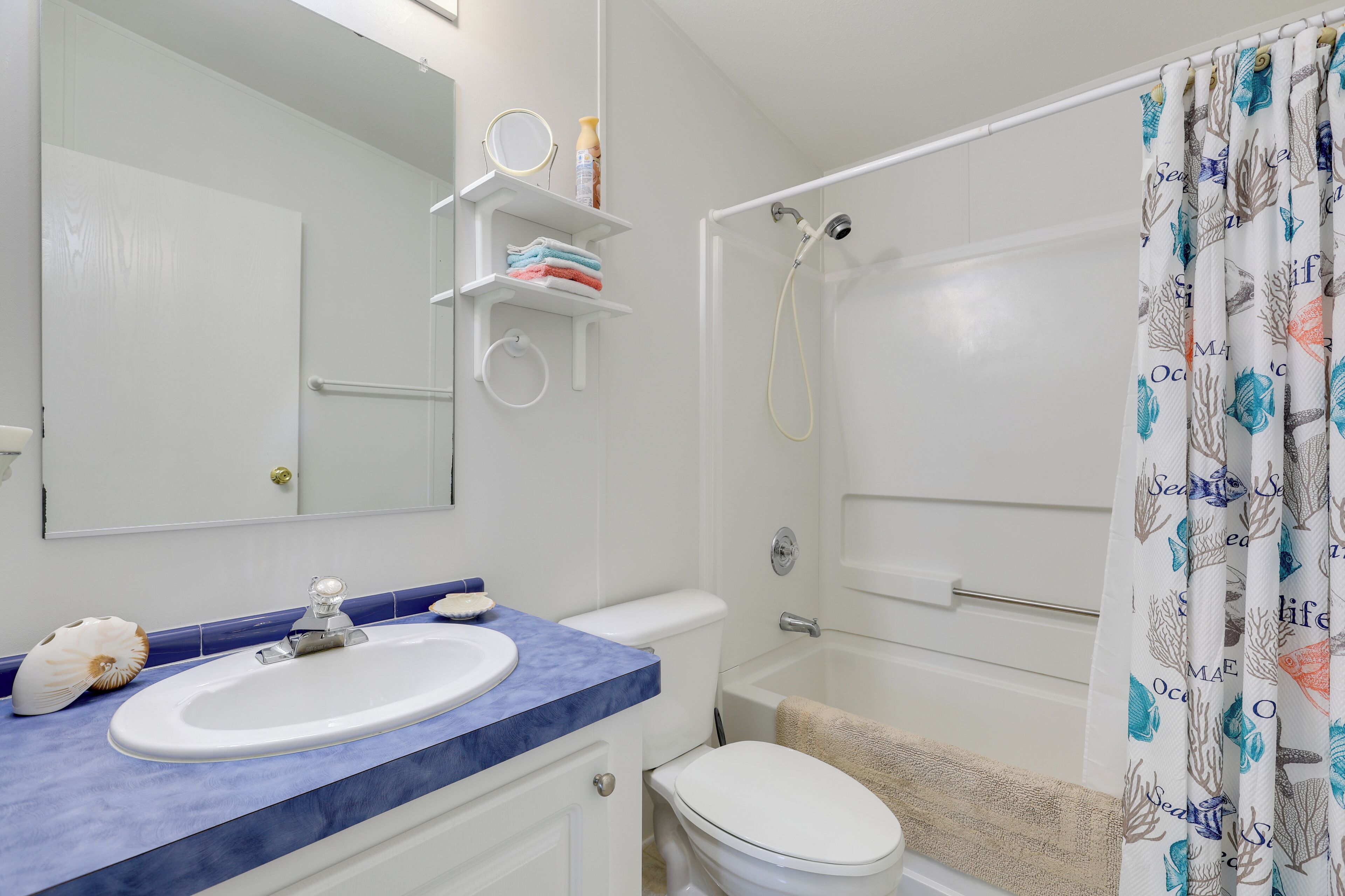 A bathroom with a white sink, blue countertop, white toilet, and a shower with a white curtain.
