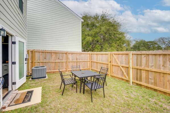 A backyard with a patio table and chairs, a wooden fence, and a house with a door. - Steps to Boardwalk & Beach! Stylish Biloxi Home (Biloxi)