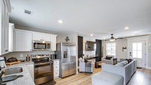 A modern kitchen with stainless steel appliances, a dining area with a sofa, and a living room with a grey couch. - Steps to Boardwalk & Beach! Stylish Biloxi Home (Biloxi)