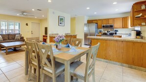 A modern kitchen with wooden cabinets, a stainless steel refrigerator, and a dining area with a wooden table and chairs.
