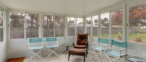 A sunroom with large windows, a brown cushioned chair, and several folding chairs.