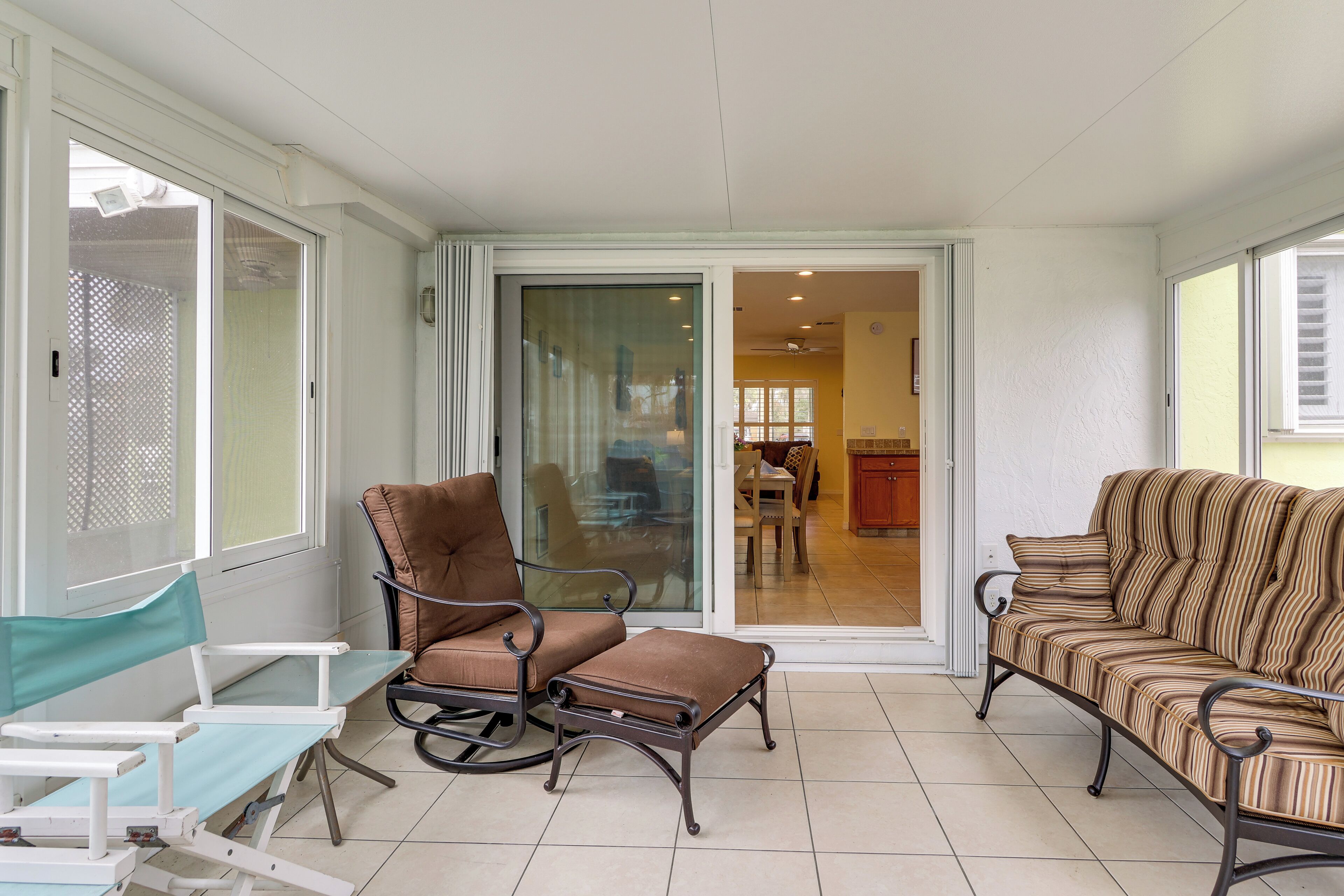 A sunlit patio area with a sliding glass door leading to a dining area, furnished with a sofa, chairs, and a small table.