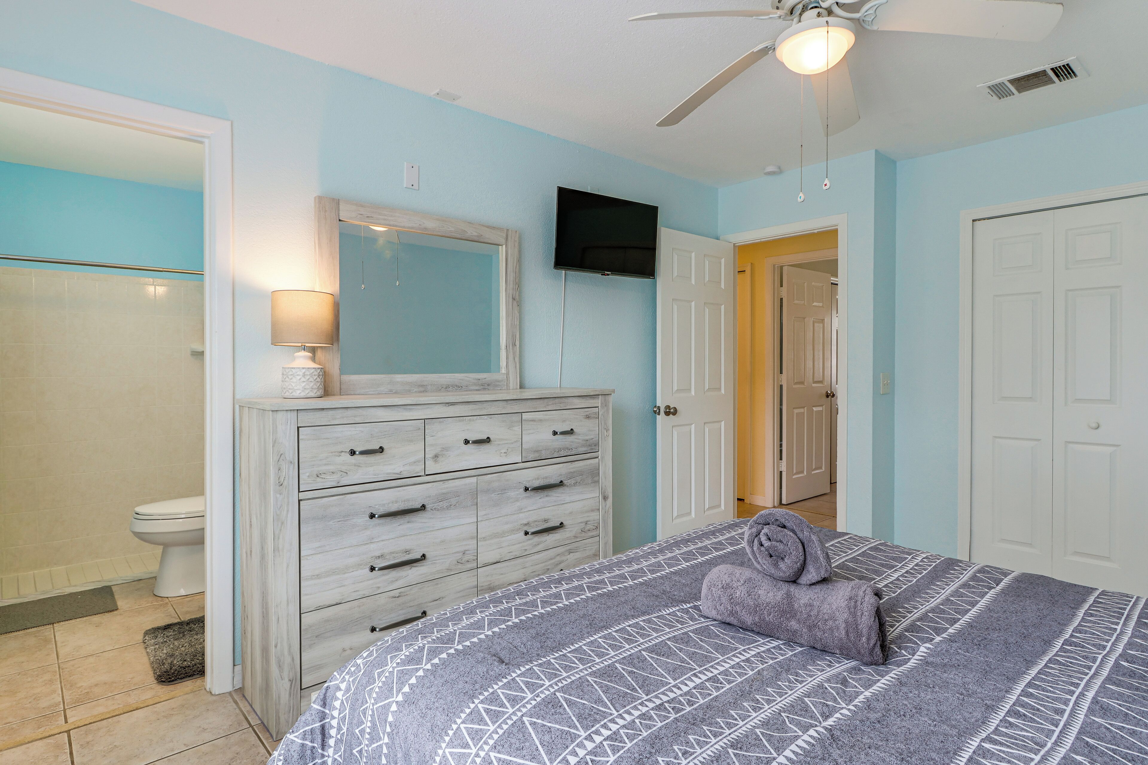 A bedroom with a bed, a dresser, a television, and a door leading to another room.