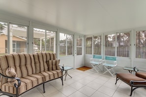 A sunroom with a striped sofa, a small table, and a folding chair.