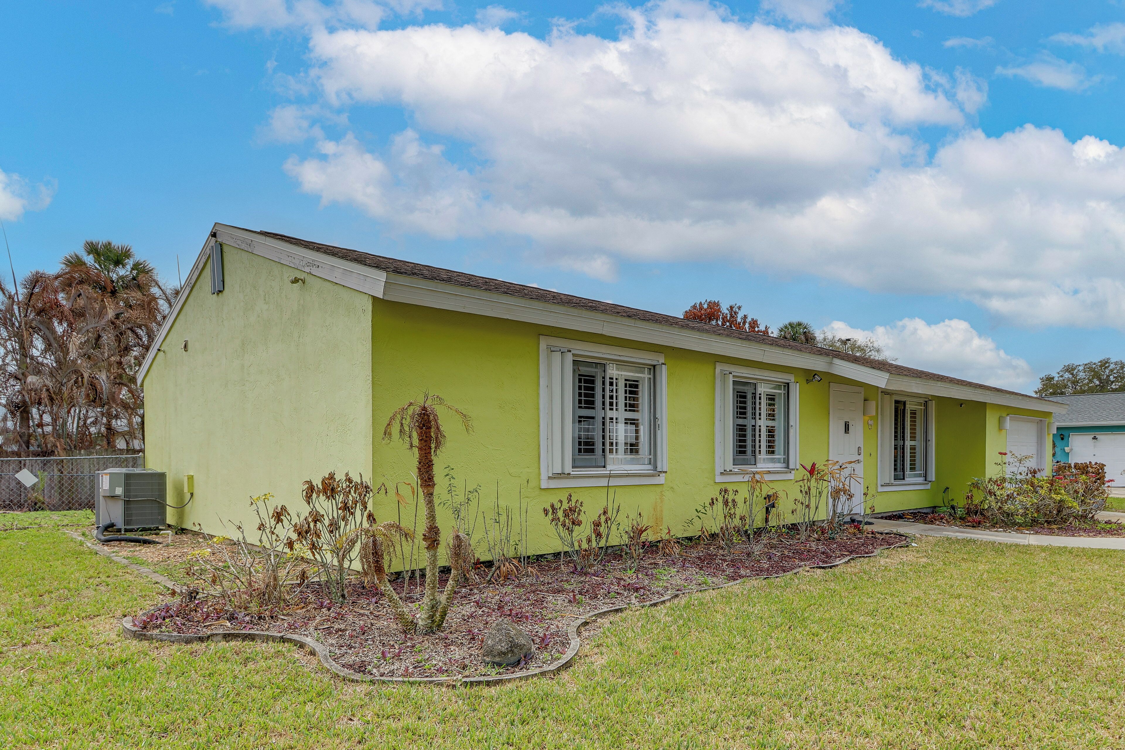 Uma casa térrea com fachada verde, detalhes brancos e um pequeno jardim frontal com canteiro e uma palmeira.