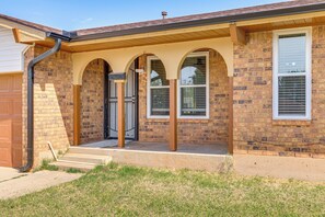 A two-story brick house with a front porch, a garage door, and a window with blinds. - 8 Mi to Bricktown Fun: Quiet Family Retreat (Oklahoma City)