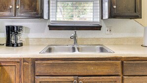 A kitchen with a double sink, wooden cabinets, a window with blinds, and a coffee maker on the counter. - 8 Mi to Bricktown Fun: Quiet Family Retreat (Oklahoma City)
