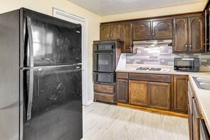 A kitchen with a black refrigerator, a microwave, a stove, and wooden cabinets. - 8 Mi to Bricktown Fun: Quiet Family Retreat (Oklahoma City)