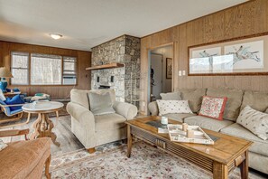 Ein gemütliches Wohnzimmer mit Kamin aus Stein, Holzboden und einem großen Fenster.