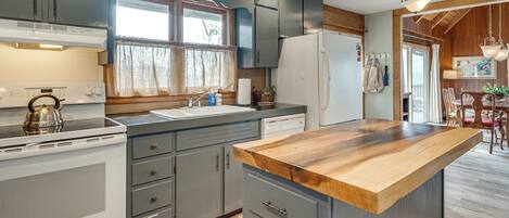 A kitchen with a wooden countertop, white appliances, and grey cabinets.
