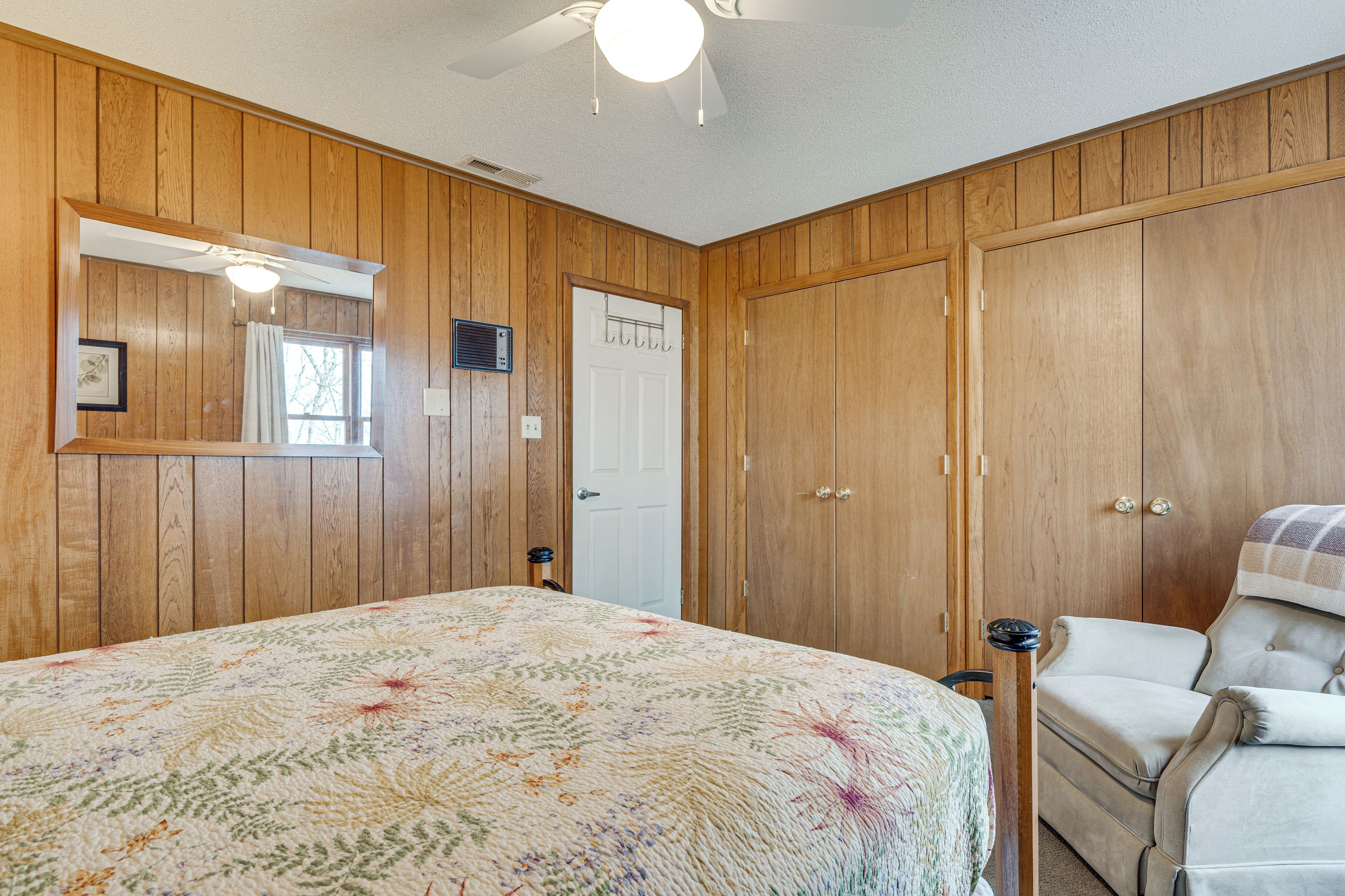 A bedroom with wooden paneling, a bed with a floral bedspread, a chair, and a wardrobe.