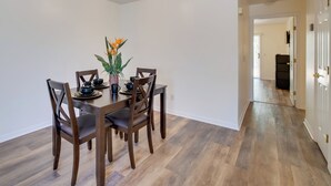 Een eethoek met een houten tafel en stoelen, een vaas met bloemen en een gang naar een andere kamer.