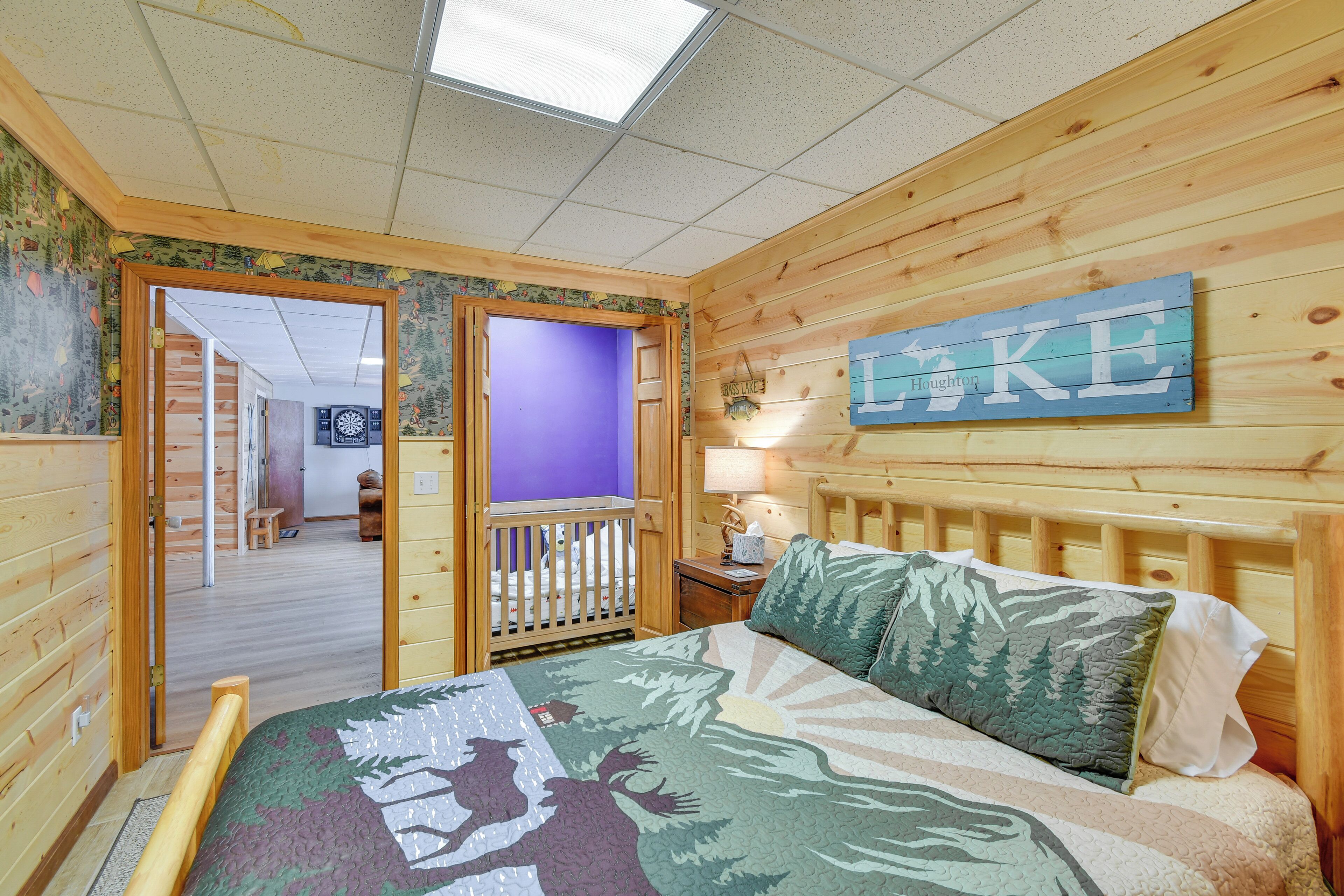 A wooden-paneled room with a bed, a crib, a wall-mounted sign, and a door leading to another room.
