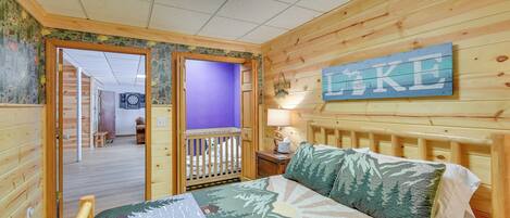 A wooden-paneled room with a bed, a crib, a wall-mounted sign, and a door leading to another room.