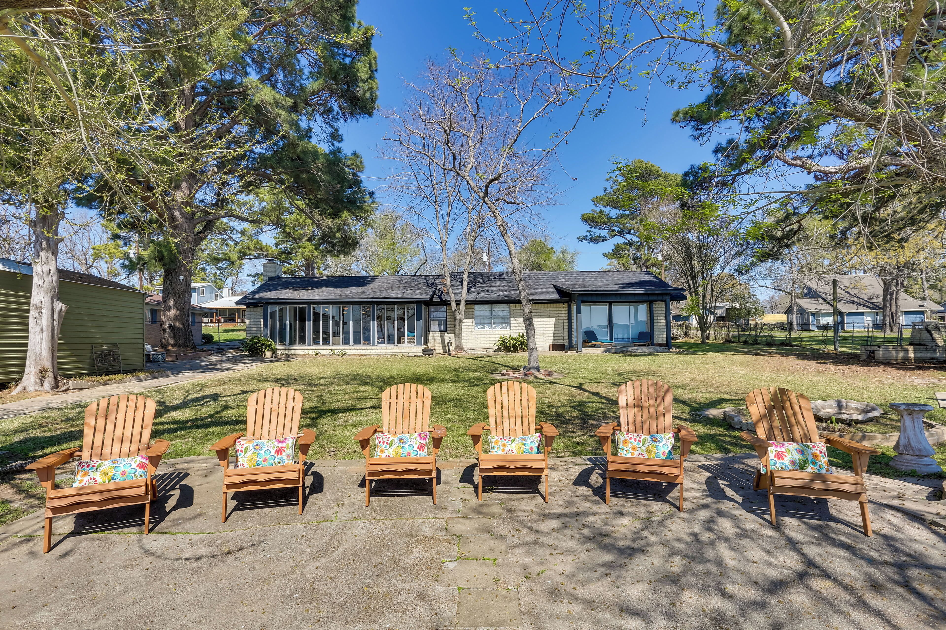 Five wooden Adirondack chairs with colorful cushions arranged on a concrete patio.