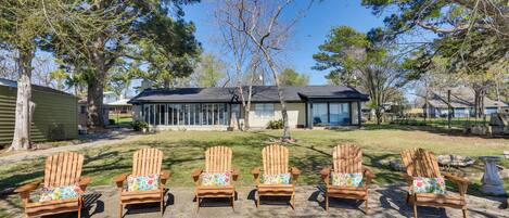 Five wooden Adirondack chairs with colorful cushions arranged on a concrete patio.