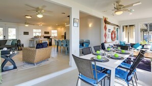 Amplia sala de estar con una mesa de comedor preparada para cuatro, un sofá y una cocina al fondo.