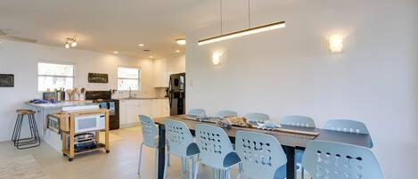 A modern kitchen with white cabinets, a microwave, and a refrigerator. There is a dining area with a table and chairs, and a sign indicating 'Jersey Tomatoes'.