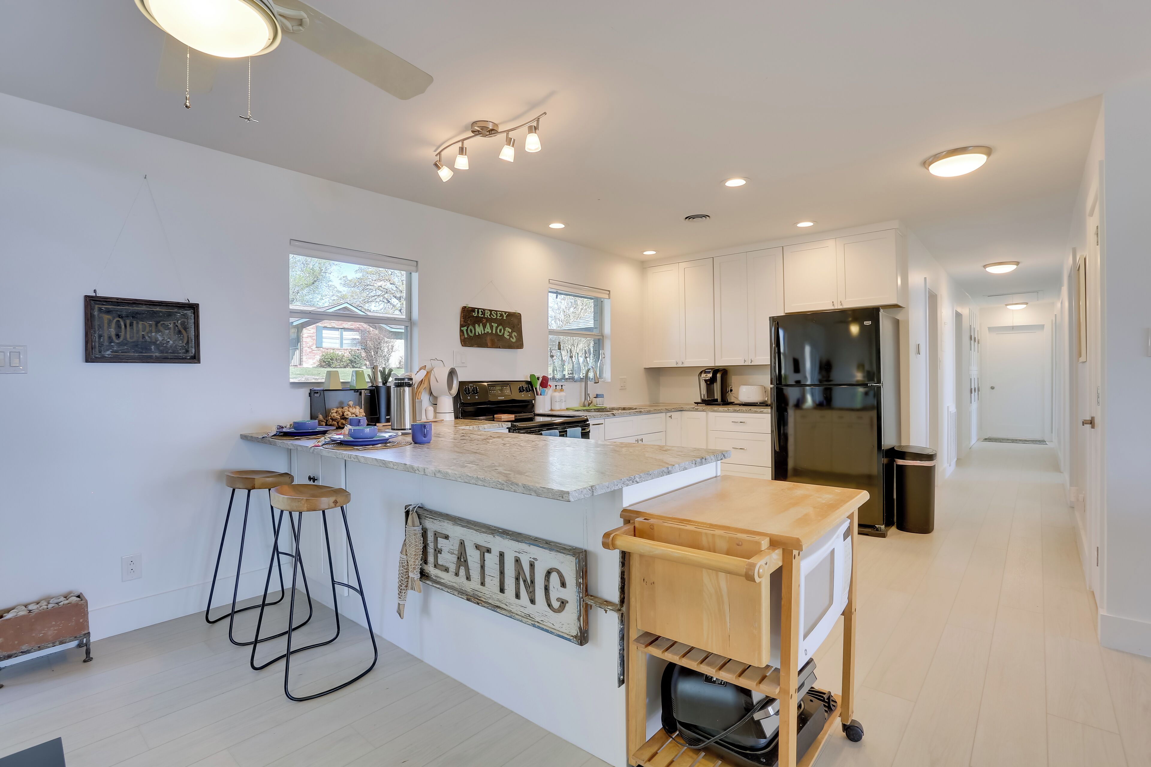 A modern kitchen with white cabinets, a central island, bar stools, and a sign that reads "EATING".