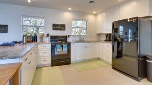 Una cocina moderna con armarios blancos, un refrigerador de acero inoxidable, una estufa negra y un letrero de pizarra.