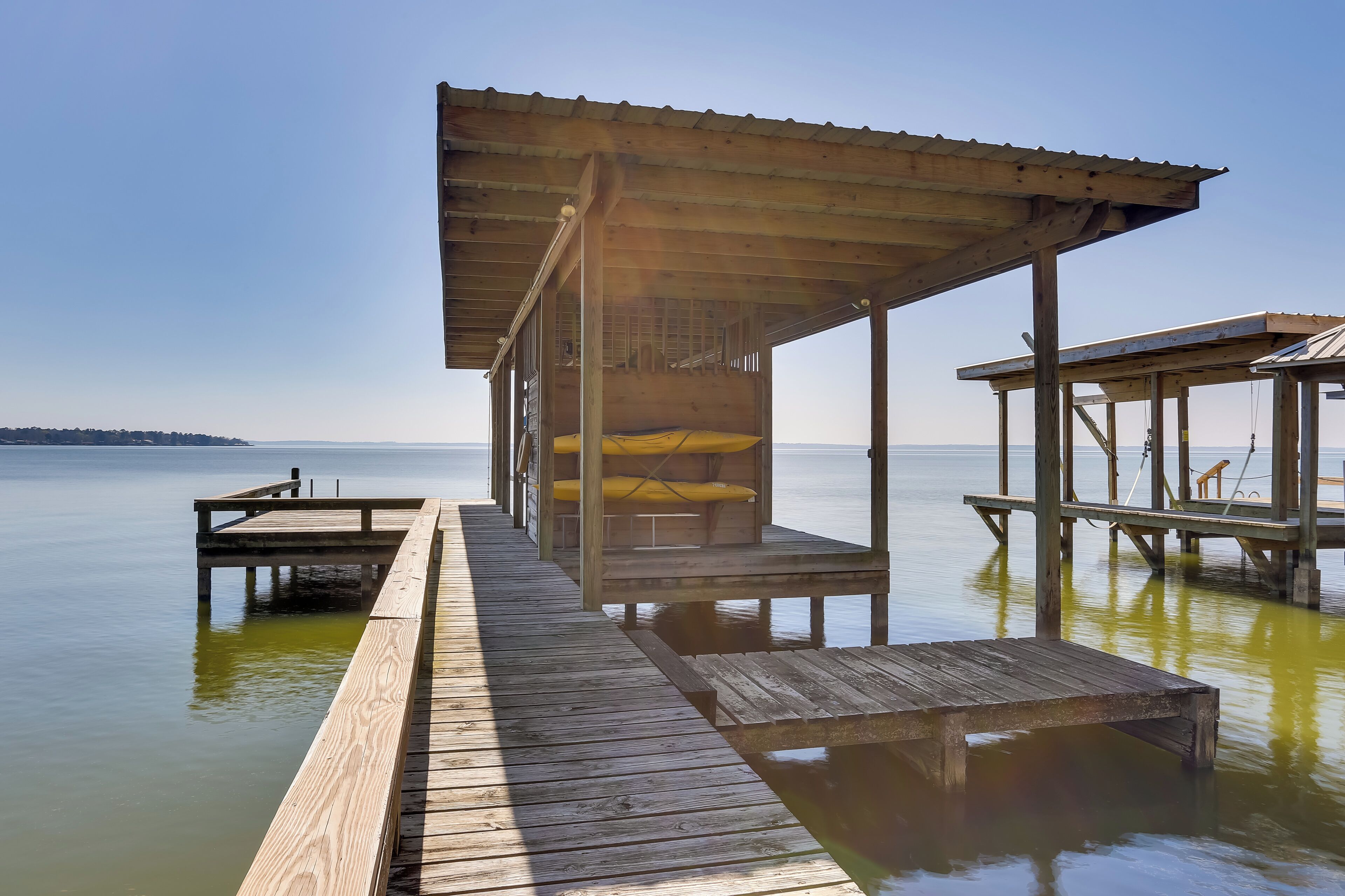Un muelle de madera se extiende sobre aguas tranquilas, con un área de descanso cubierta y un pequeño bote amarrado cerca.