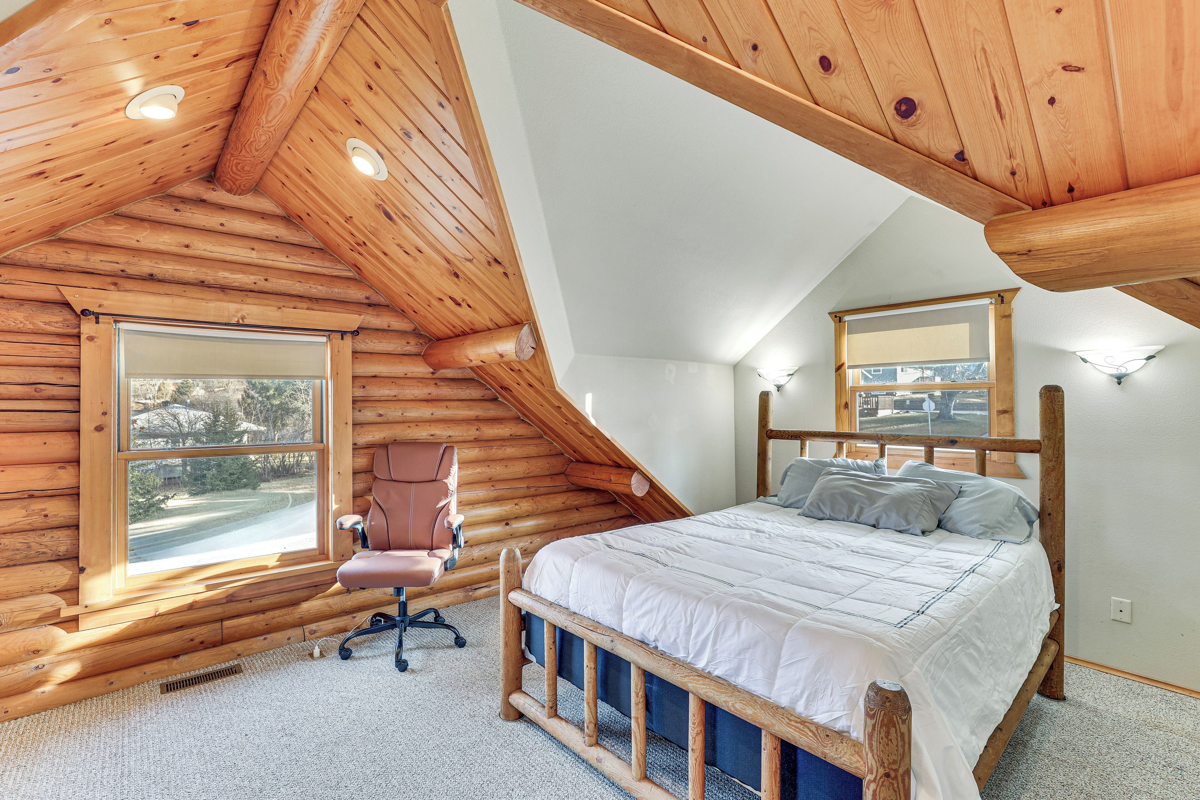 A log cabin bedroom with a wooden bed, a chair, and a window.