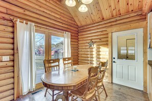 A wooden cabin interior with a round dining table, four wooden chairs, a white door, and a star decoration on the wall.