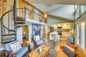 A spacious living area with a curved staircase, a fireplace, and a kitchen in the background. - Hike, Fish & Unwind: Cocolalla Lake Home w/ Dock! (Cocolalla)