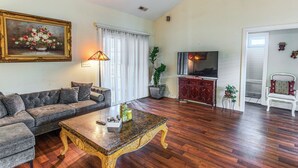 A living room with a sofa, a coffee table, a painting, a lamp, a television, and a cabinet. - Screened Porch + Pool Access: Longs Golf Getaway (Longs)